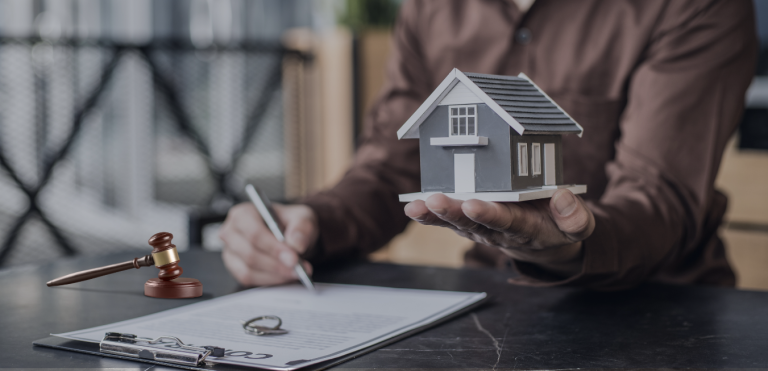A person signing a real estate agreement holding house model in the hand